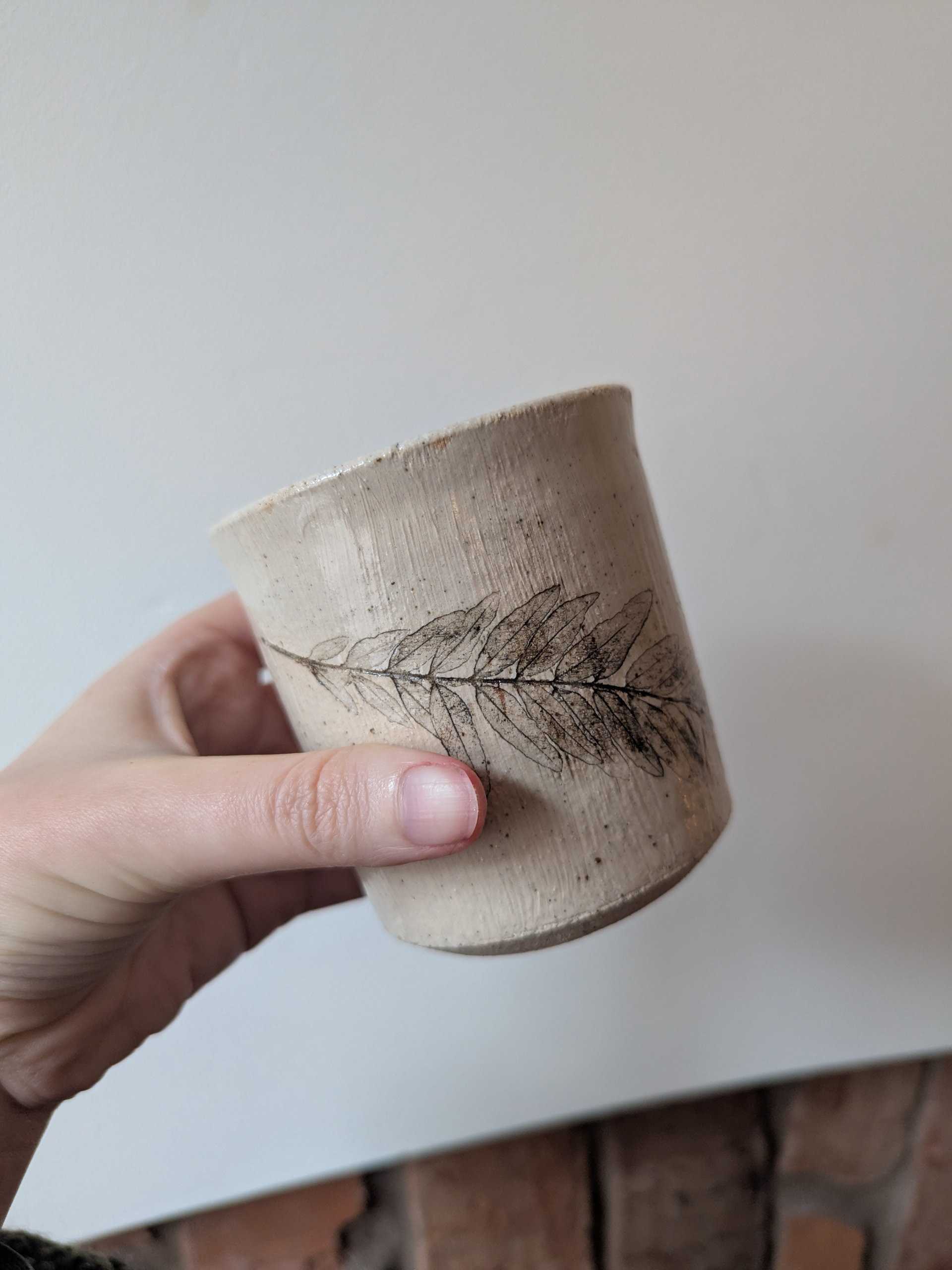 Cup with delicate leaf etching held in a hand
