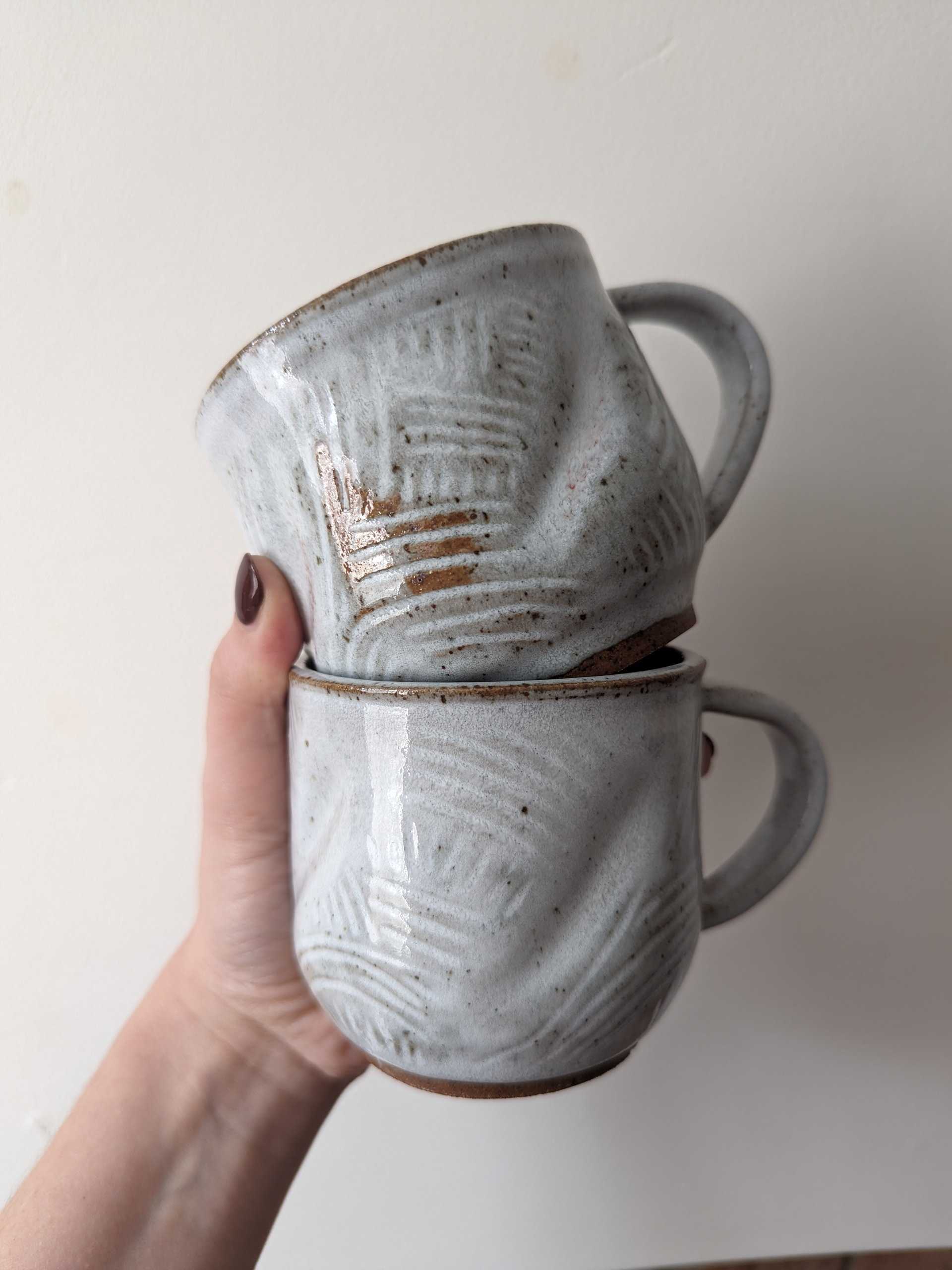 Two white stoneware mugs stacked, with brush texture